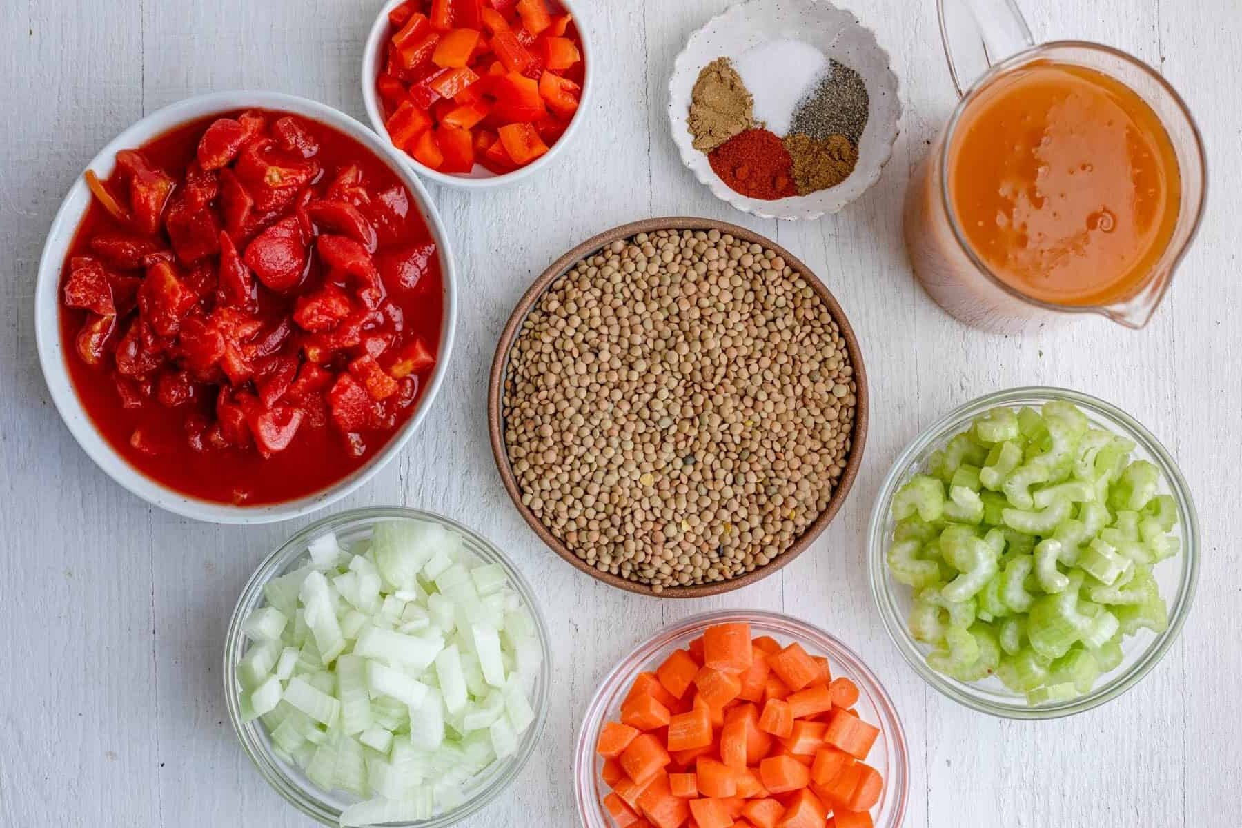 Ingredients for soup recipe: dried lentils, broth, sliced celery, diced carrots, diced onions, seasonings, canned chopped tomatoes, and diced red peppers.