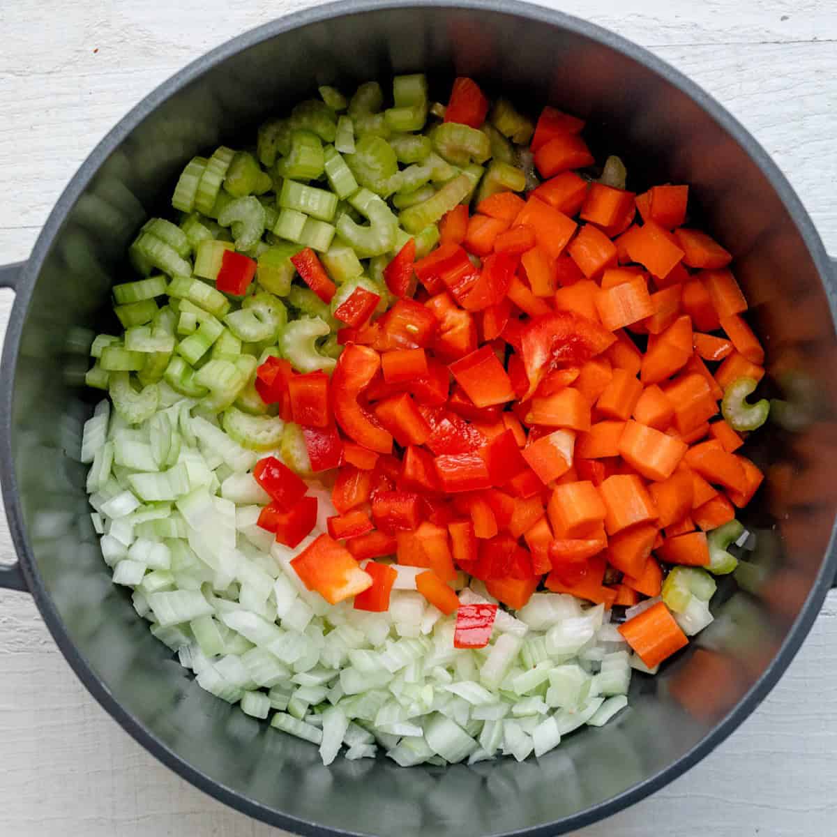 Onions, carrots, celery, bell pepper, and garlic in pot.