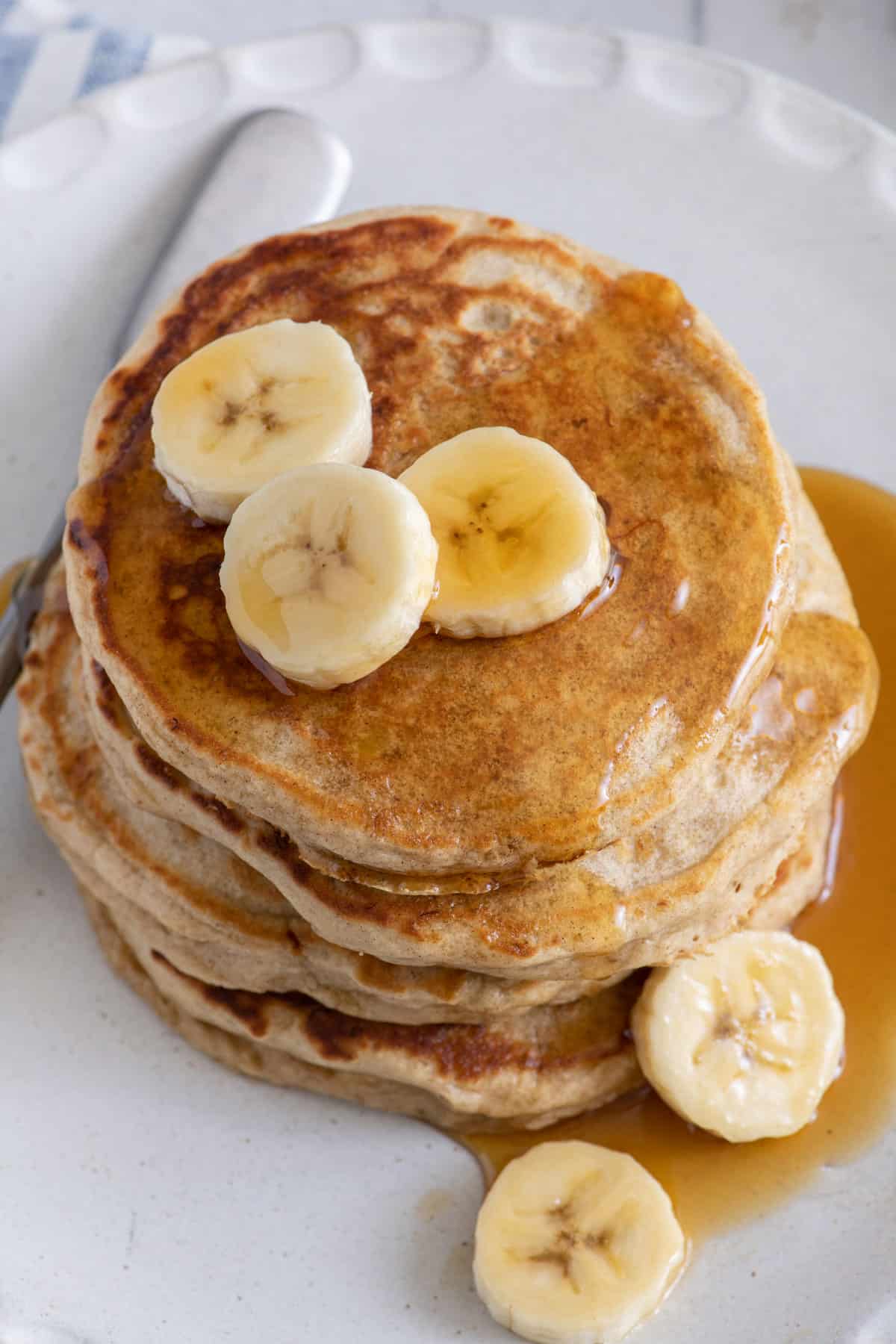 Overhead shot of a stack of banana pancakes with maple syrup and sliced bananas.