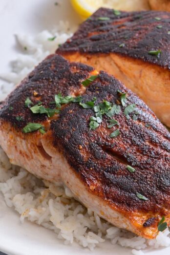 Cooked salmon on plate garnished with parsley and lemon wedges.