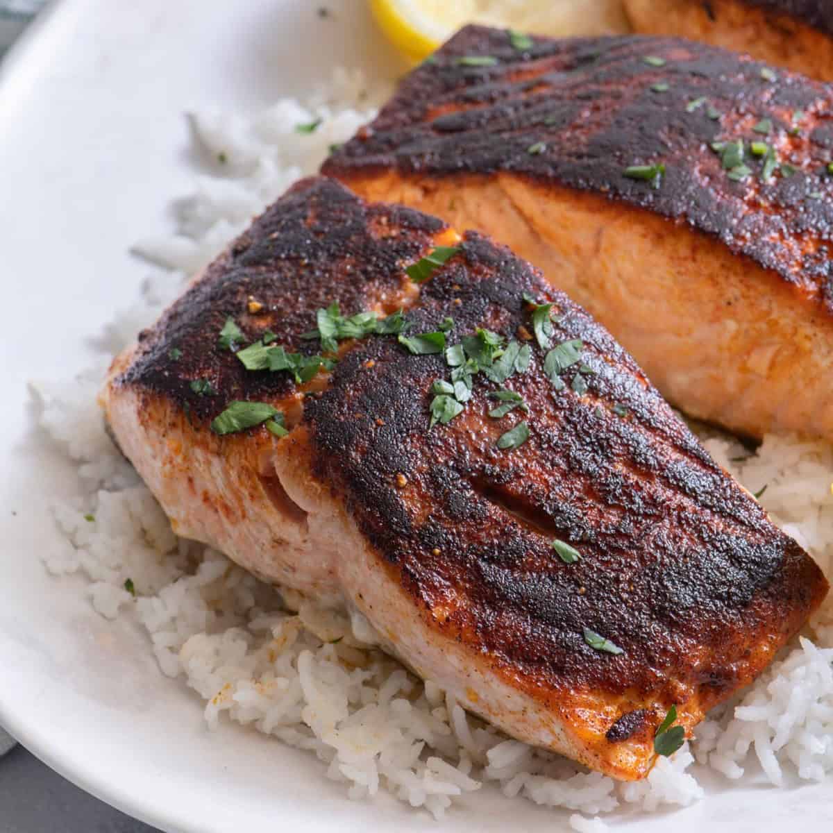 Cooked salmon on plate garnished with parsley and lemon wedges.