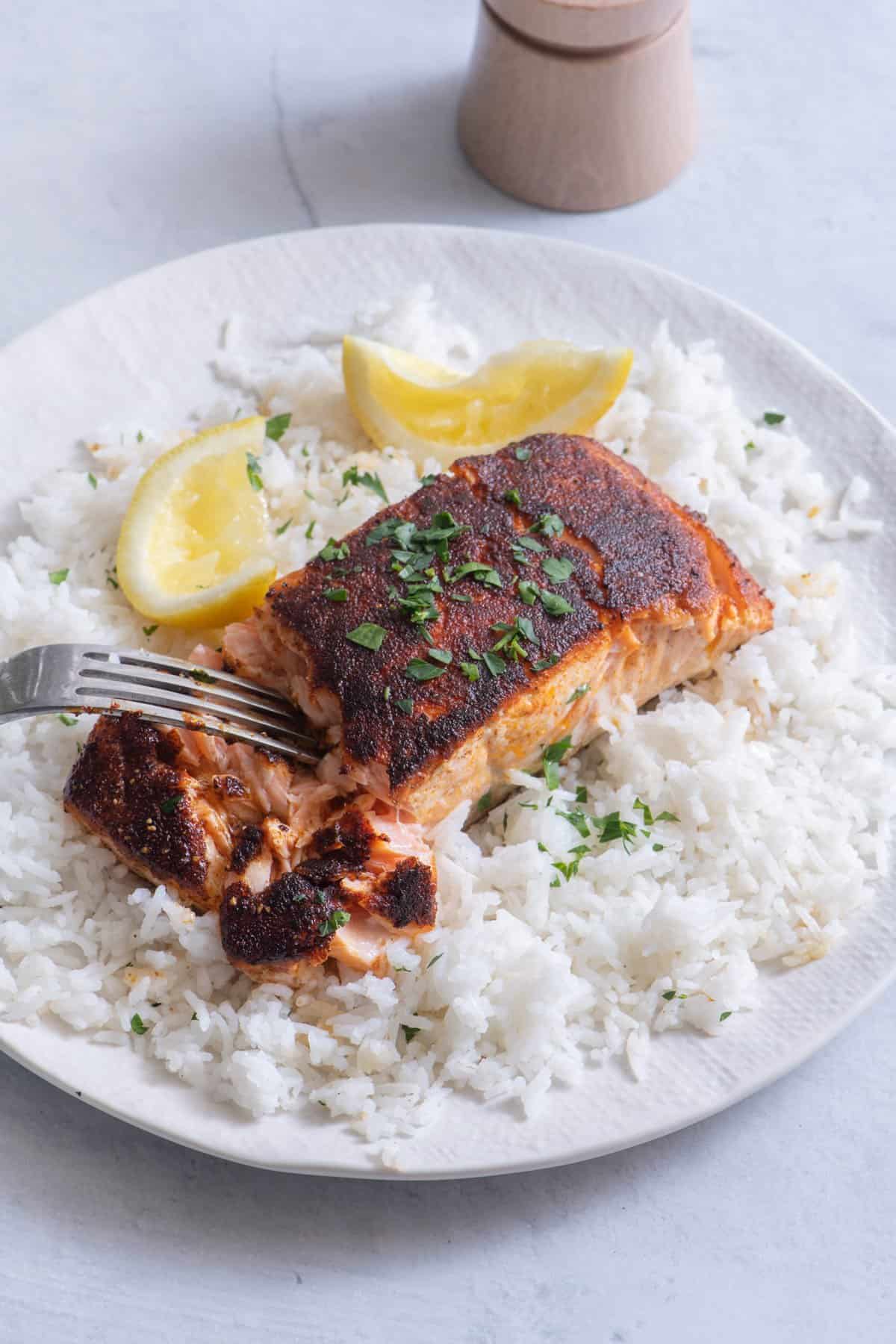 Salmon filet with fork flaking the side of fish sitting ontop of white rice.