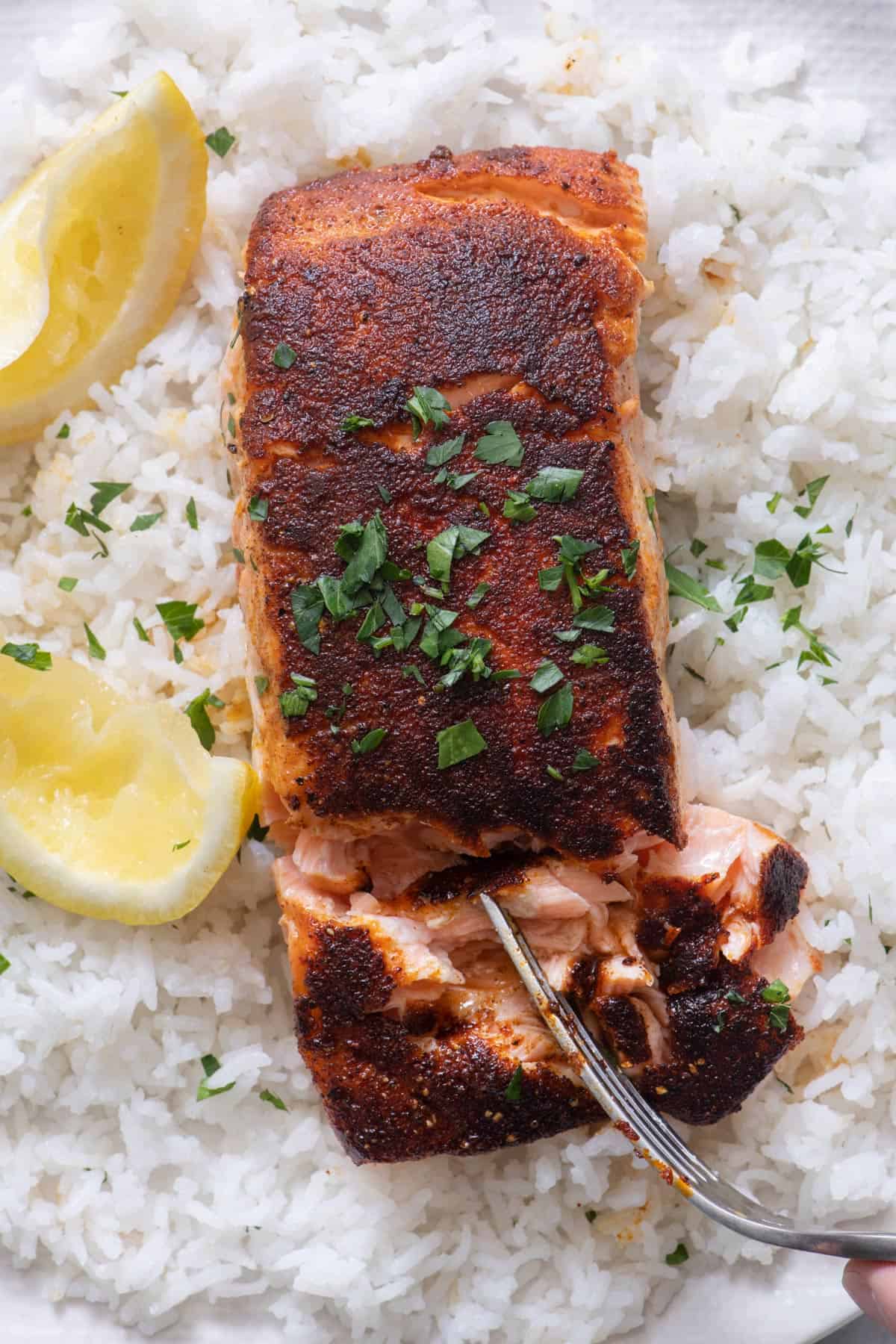 Close up of fork flaking salmon on a bed of white rice with lemon wedges and parsley.