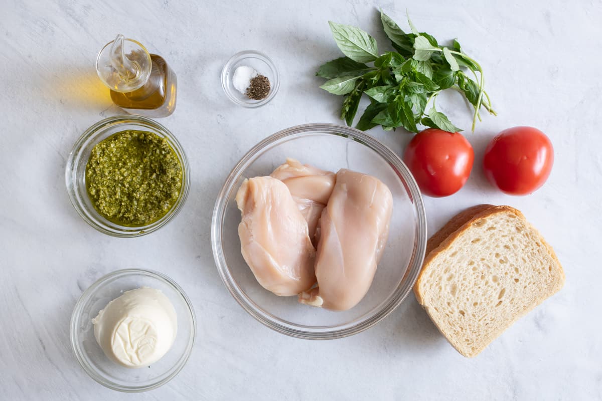 Ingredients for recipe: oil, pesto, mozzarella, salt, pepper, chicken breast, fresh basil, whole tomatoes, and sliced bread.