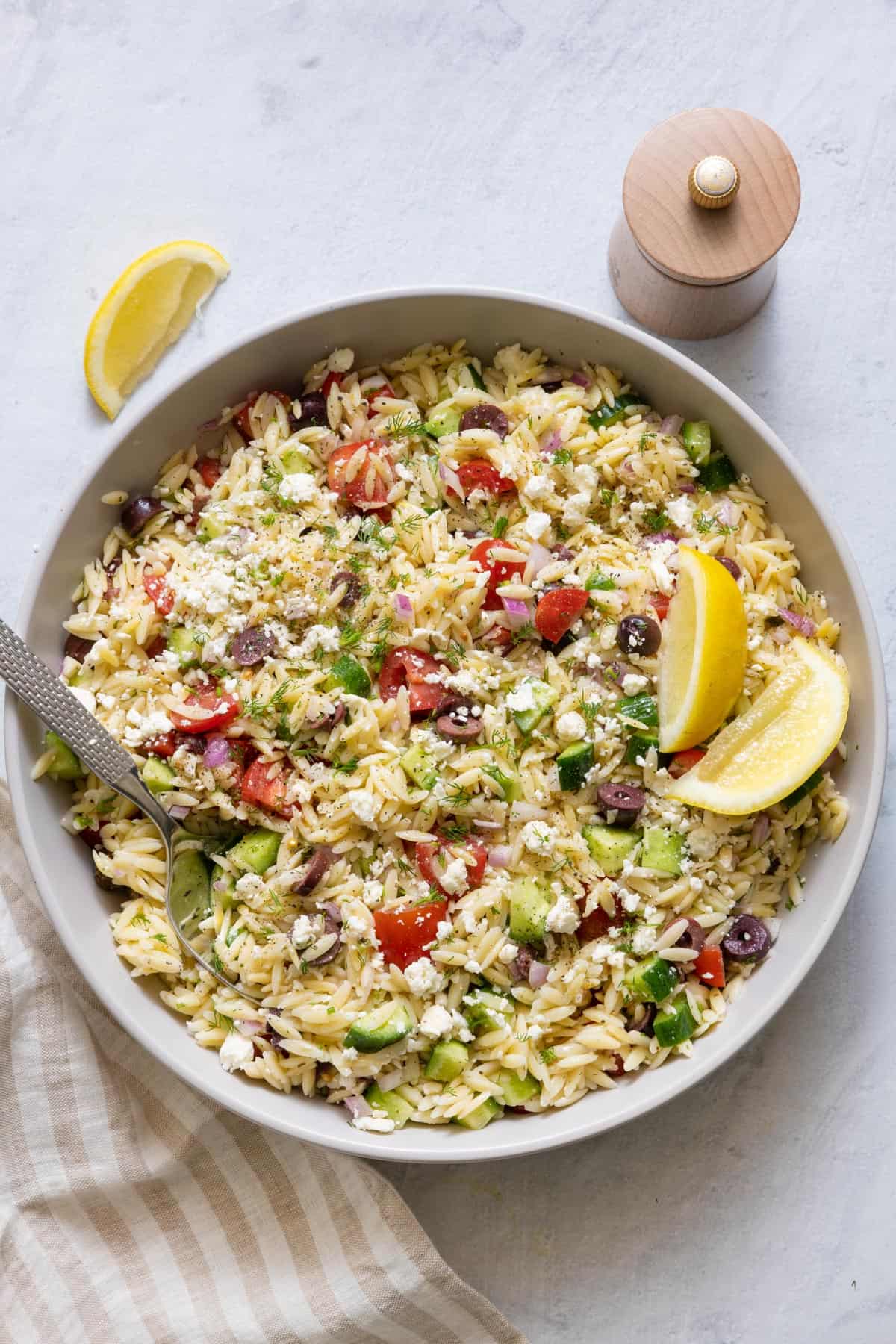 Large bowl of orzo salad with a dipped spoon and garnished with lemon wedges.