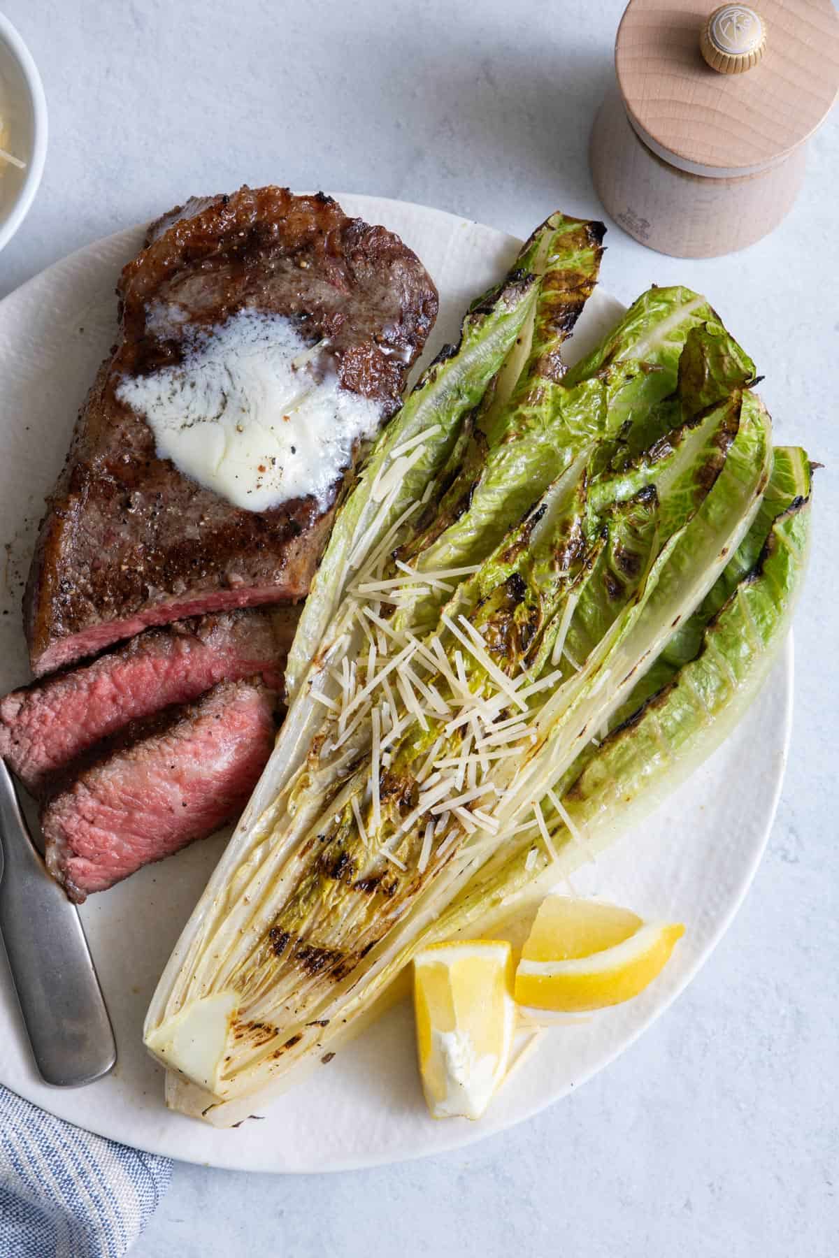Grilled romaine lettuce garnished with shredded parmesan served with grilled steak with butter on top.
