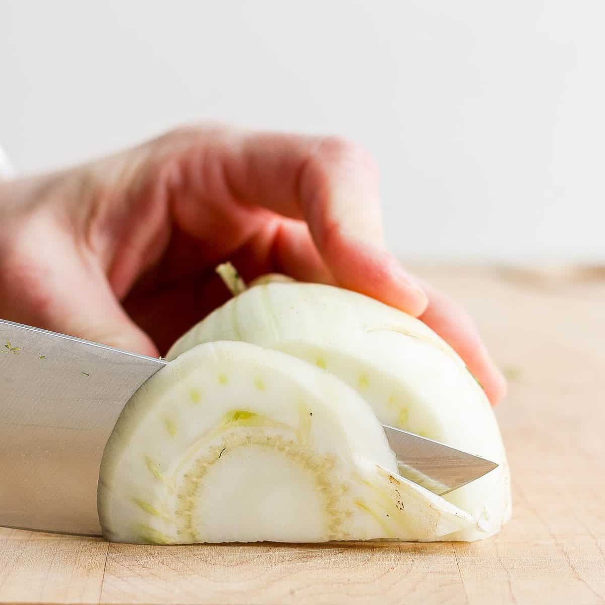 Cutting half of a fennel into thin slices.