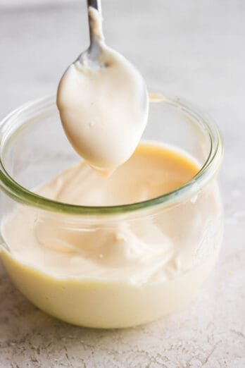 Spoon dipping out fresh made mayonnaise from glass jar.