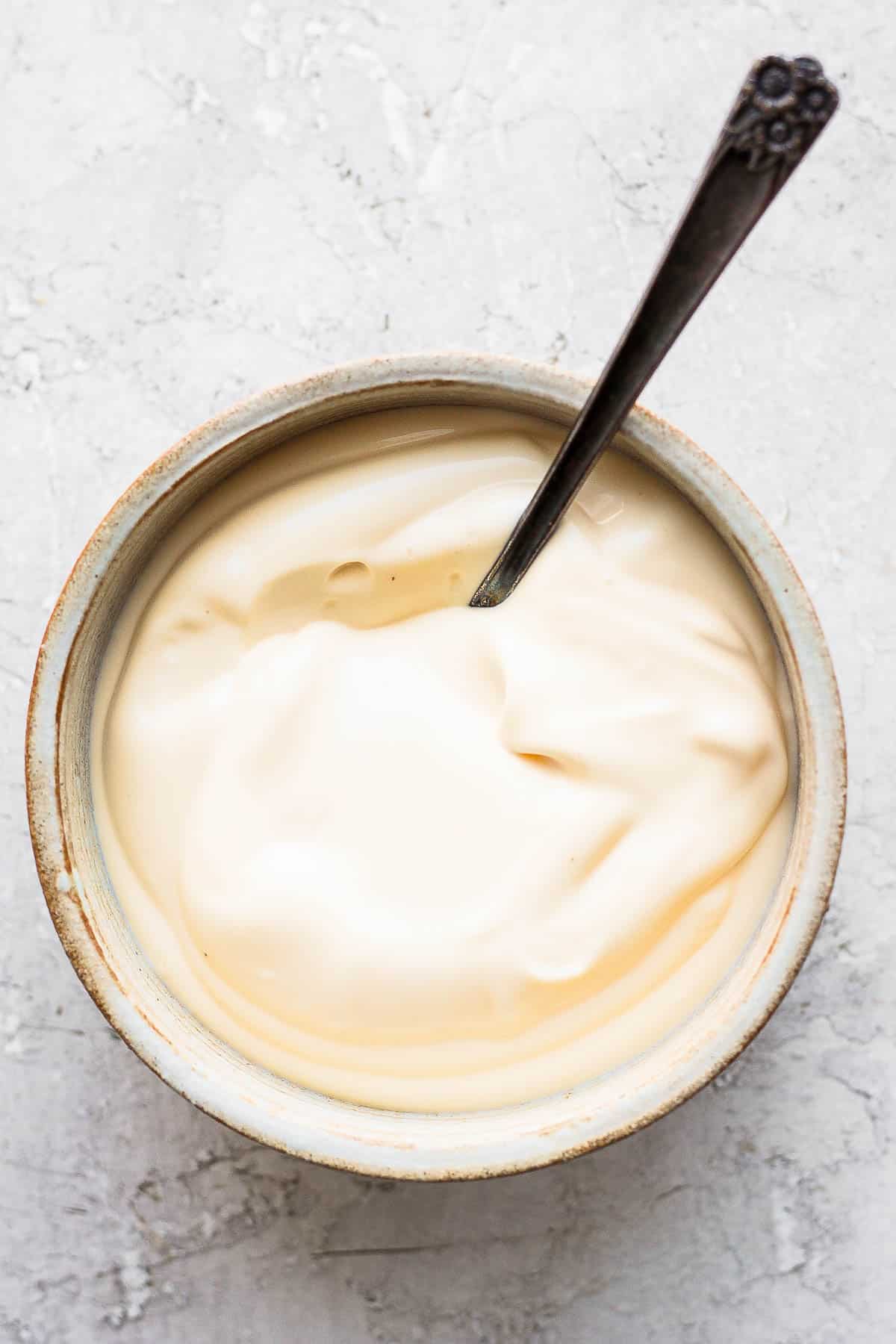 Overhead shot of a bowl of mayonnaise with spoon dipped inside.
