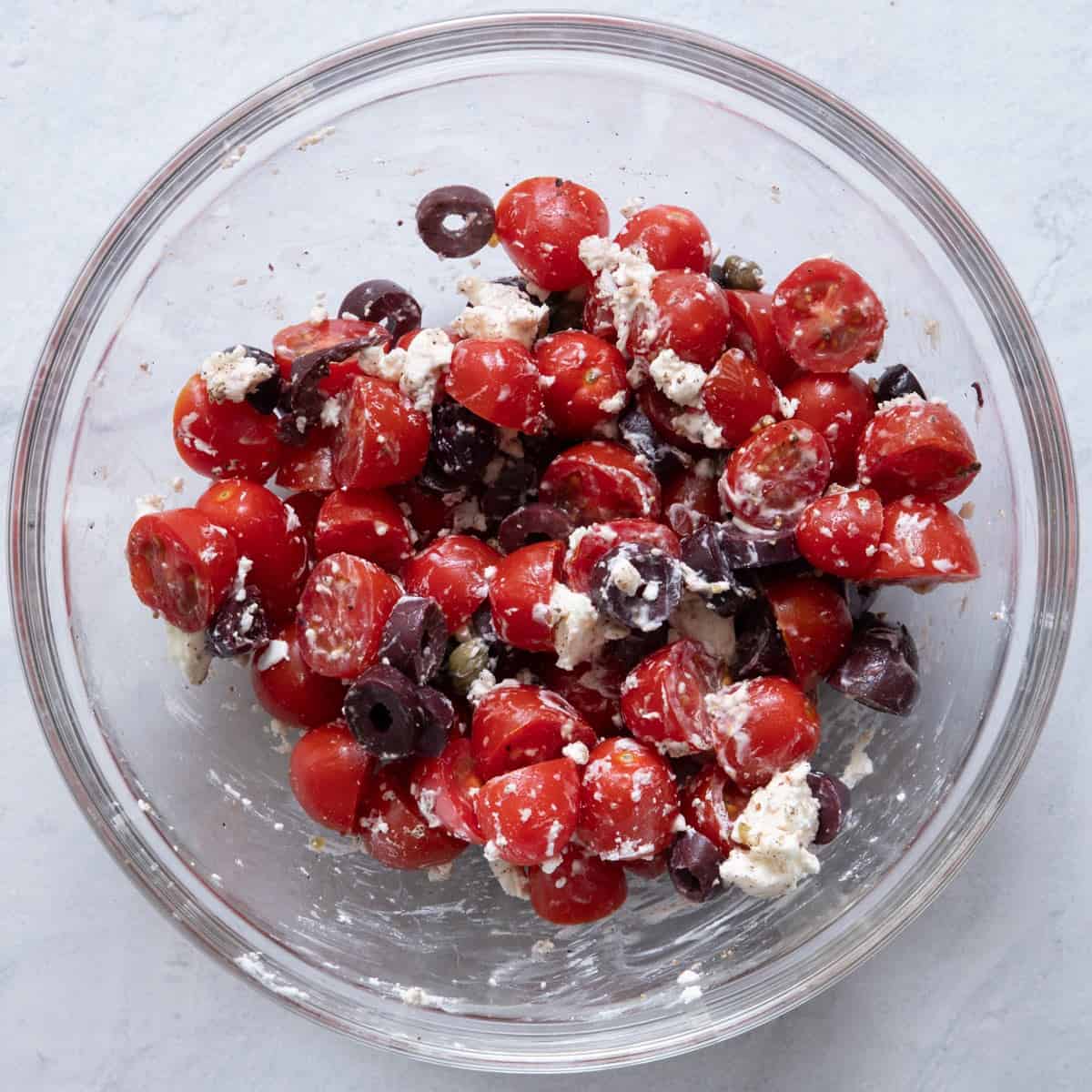Tomatoes, olives, feta cheese, capers and black pepper in large bowl after mixed.