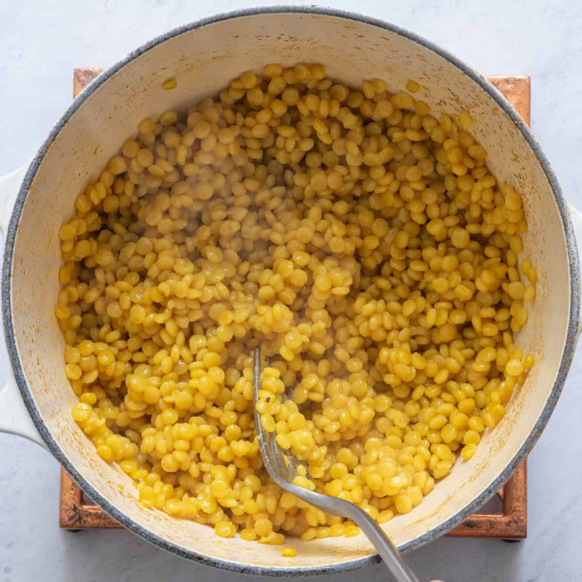 Couscous and broth in skillet after cooked, fluffing with fork.
