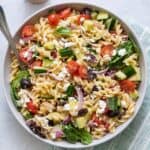 Mediterranean pasta salad in a serving bowl with a spoon resting inside.