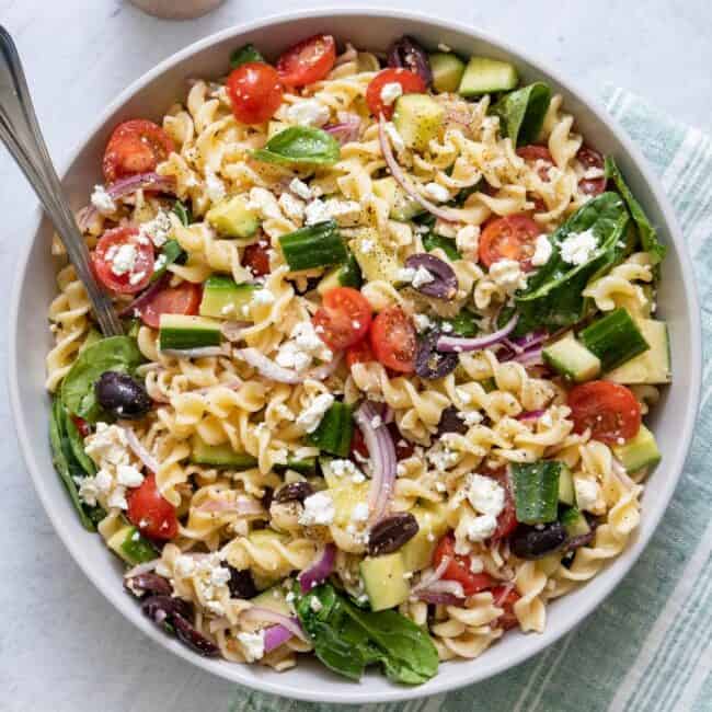 Mediterranean pasta salad in a serving bowl with a spoon resting inside.