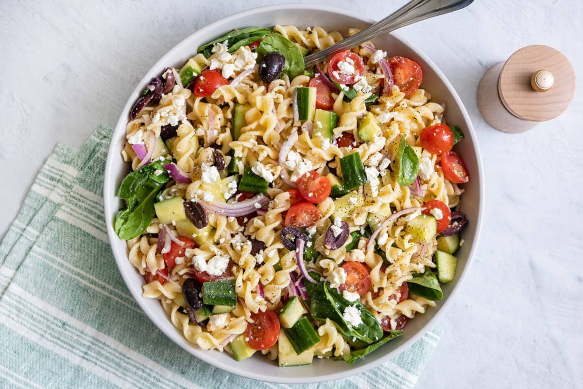 Mediterranean pasta salad in a serving bowl with a spoon resting inside. 