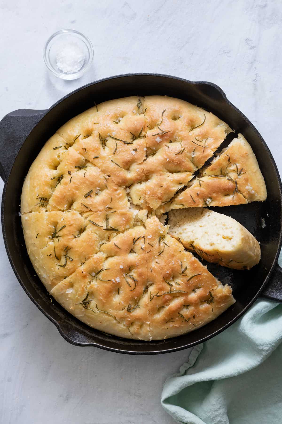 Focaccia in skillet cut into 8 slices with one slice flipped over to show texture.