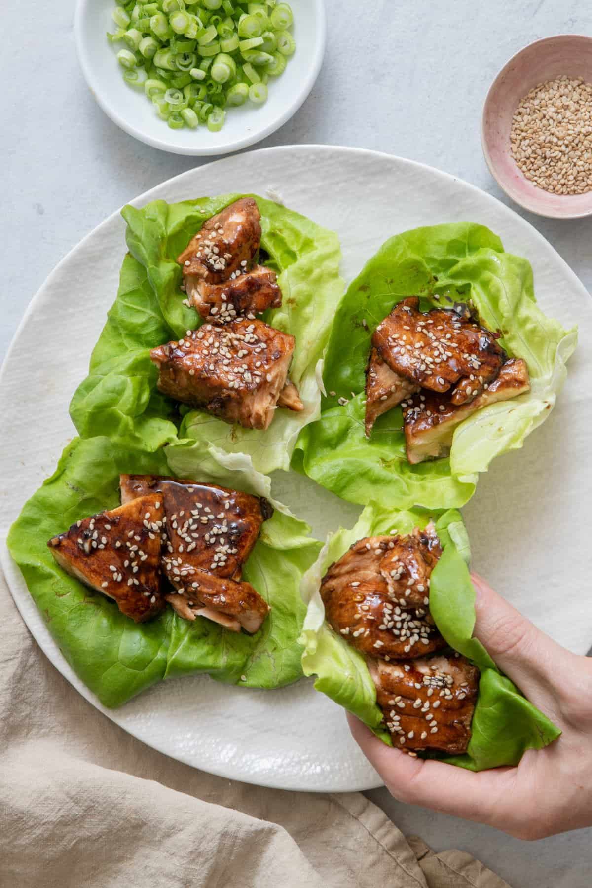 Hand grabbing lettuce wraps from plate with 3 more on plate.
