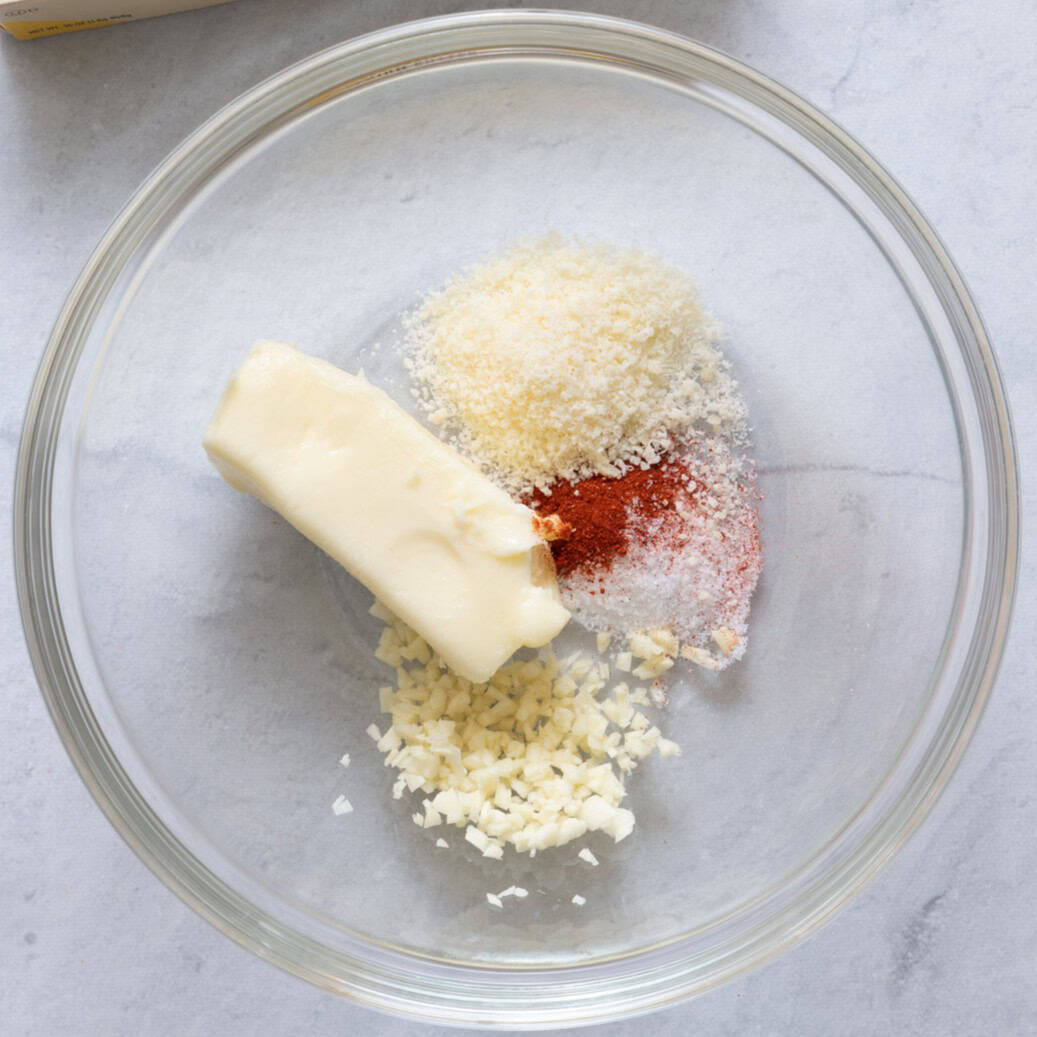 Softened butter in bowl, with garlic, salt and paprika on top before mixing.