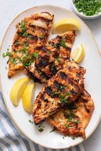 Over head shot showing 4 grilled chicken breasts on plate garnished with lemon wedges and parsley.