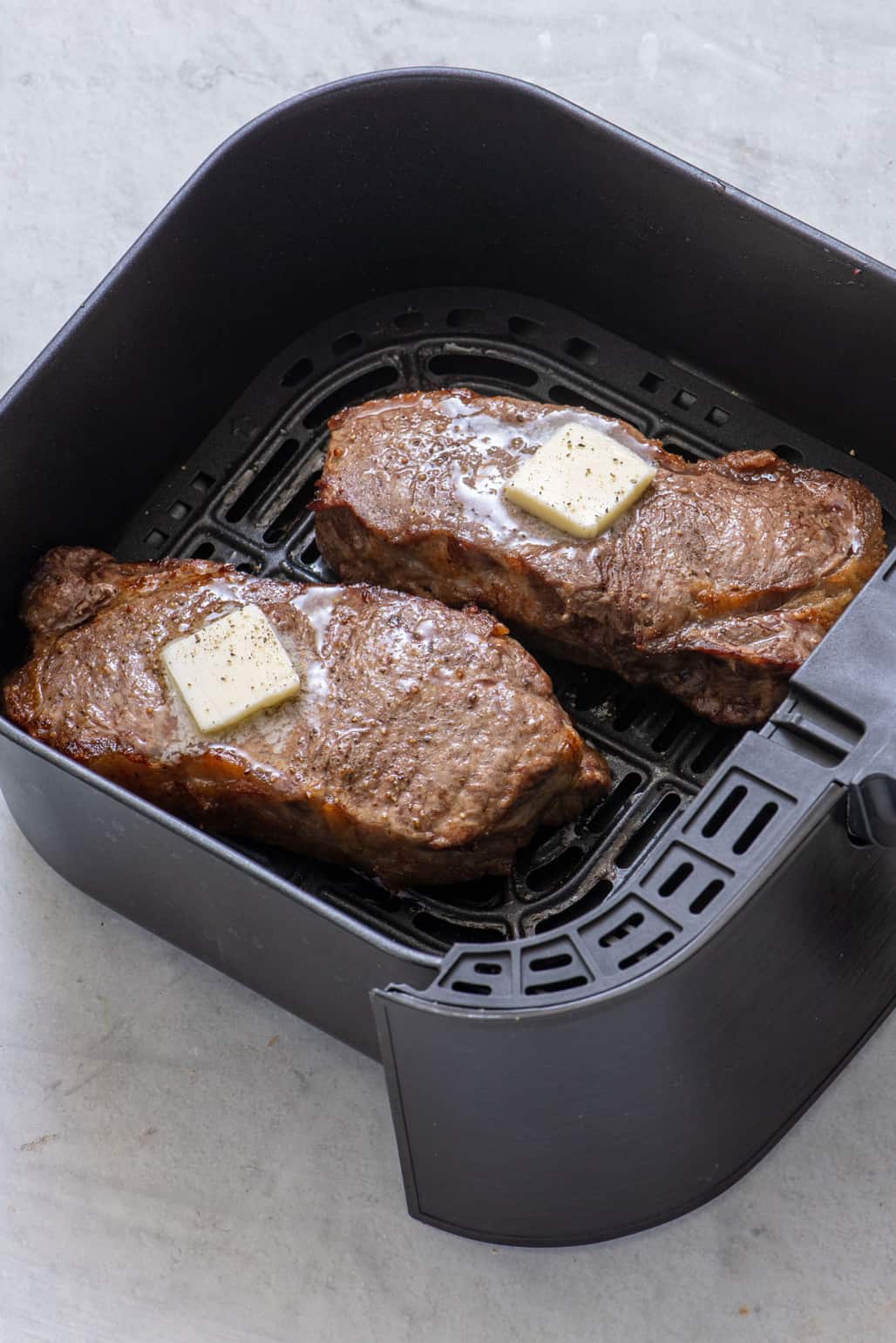 2 steaks in air fryer with melted butter, salt, and pepper after being cooked.