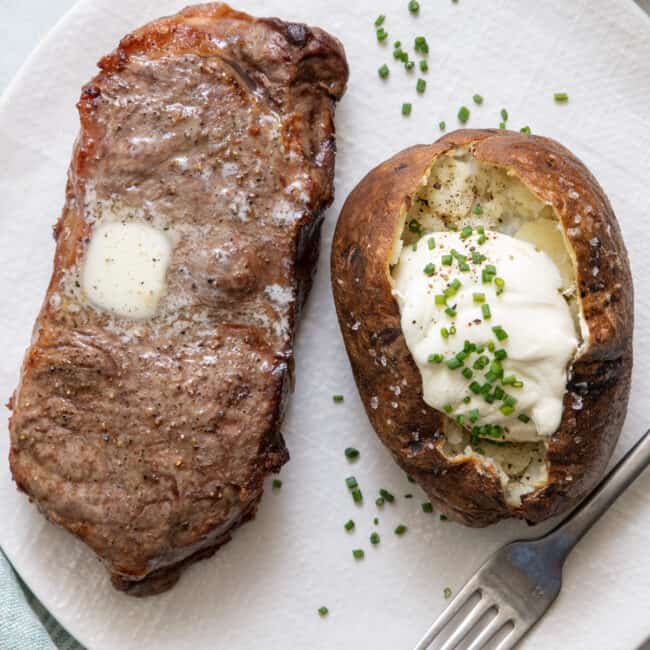 Air fryer steak on a textured plate with melted butter on top next to baked potato topped with sour cream and chives.