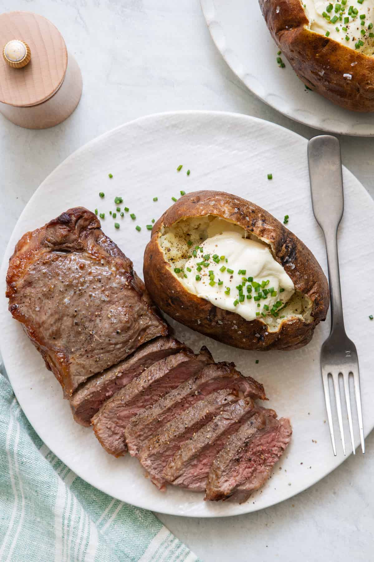 Steak cooked medium sliced half way to show color on plate next to potato with sour cream and chives.