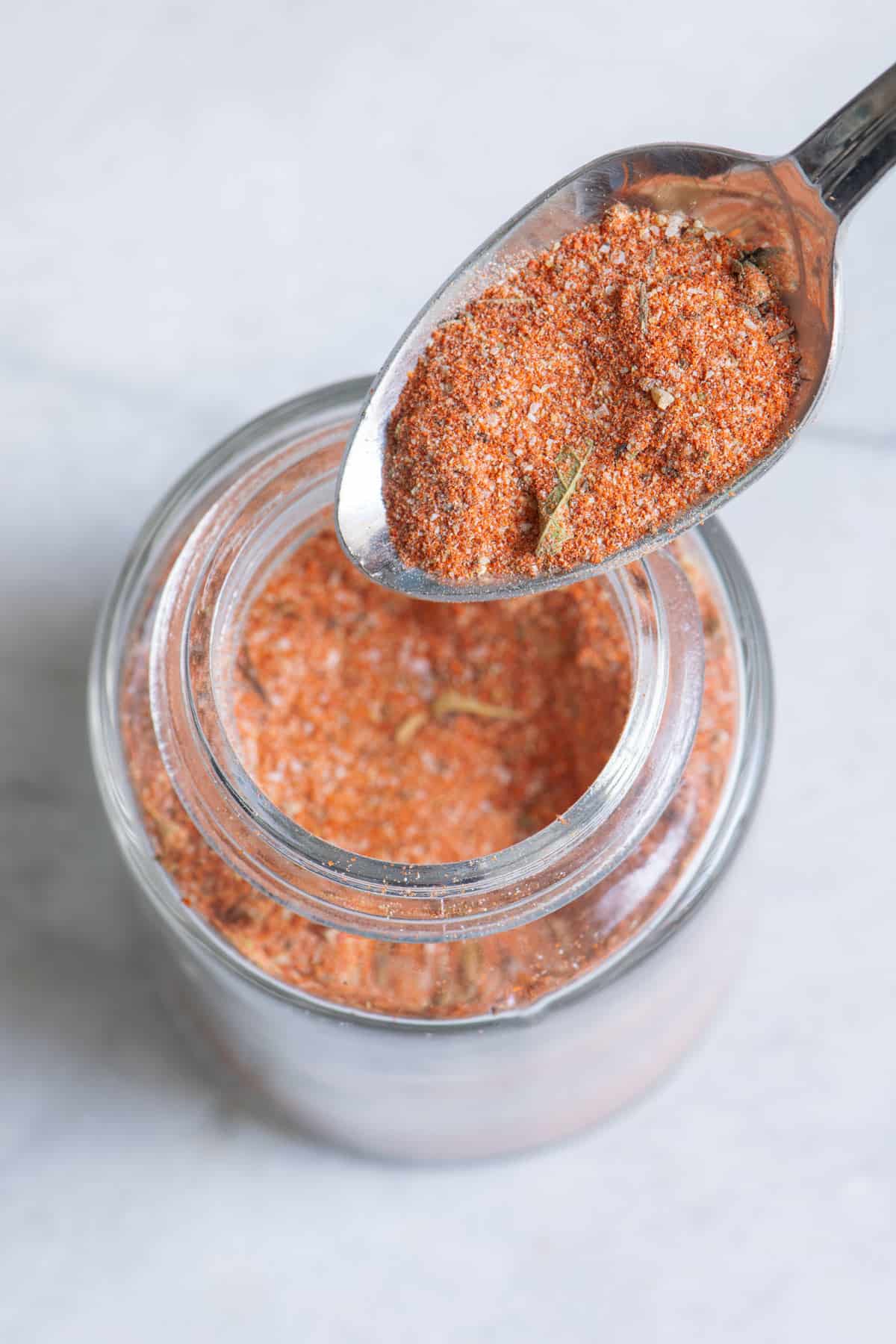 Top down shot of a spoon with Cajun seasoning and a jar of the seasoning underneath.