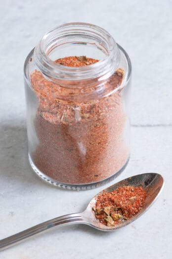 Glass jar of cajun seasoning with a spoon next to the jar and some of the seasoning on it.