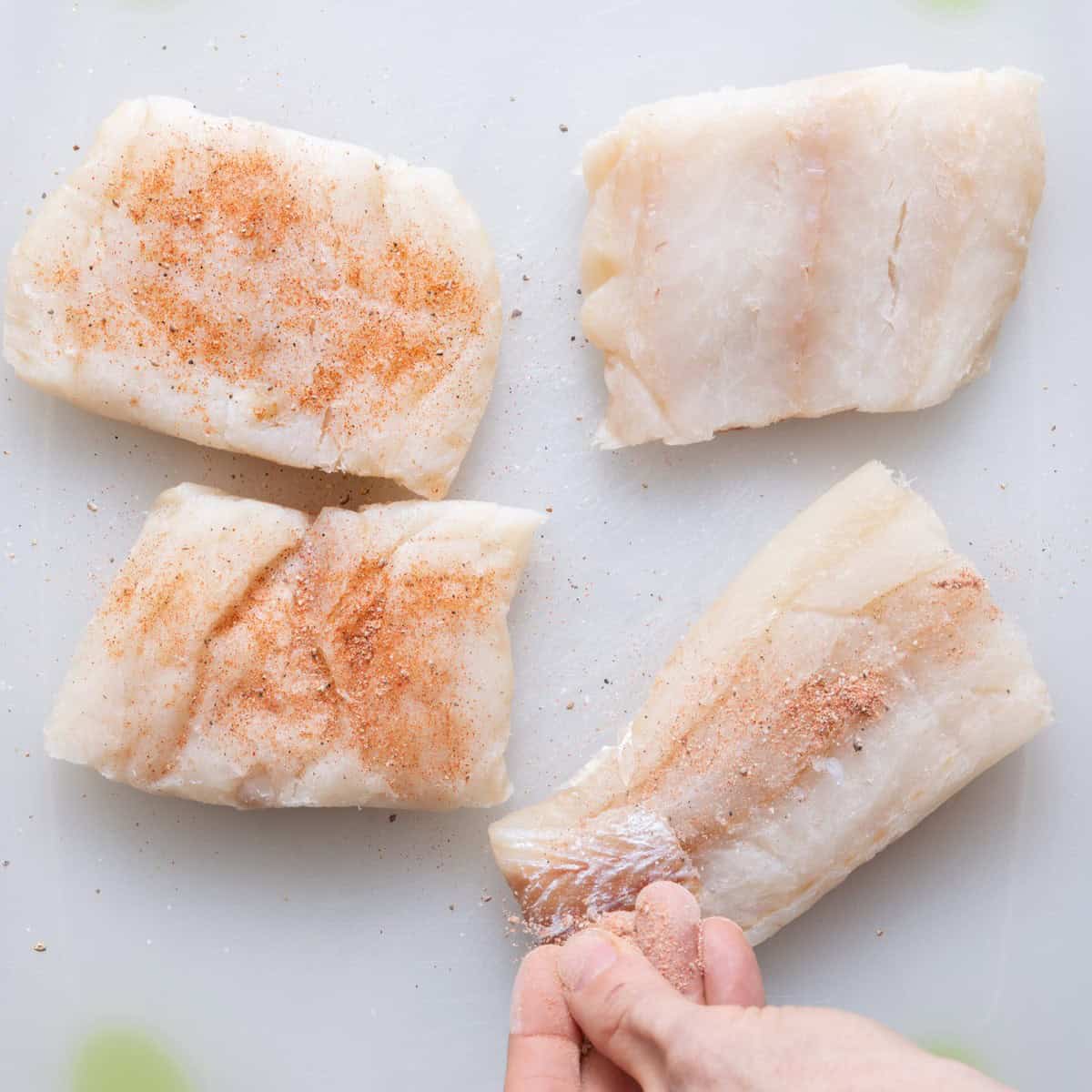 Sprinkling seasoning on cod.