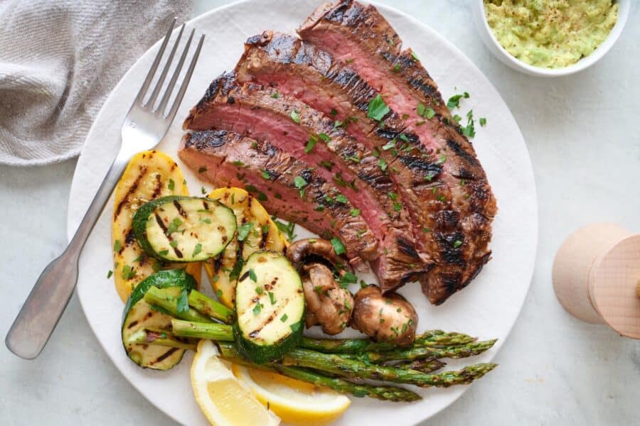 Grilled flank steak on a plate with grilled vegetables.
