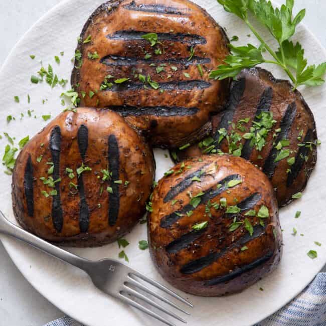4 grilled mushrooms on a plate garnished with chopped parsley.