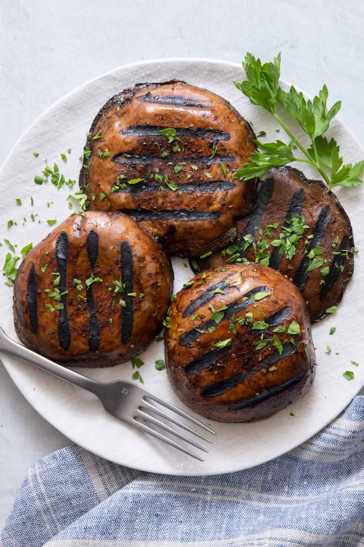 4 grilled mushrooms on a plate garnished with chopped parsley.