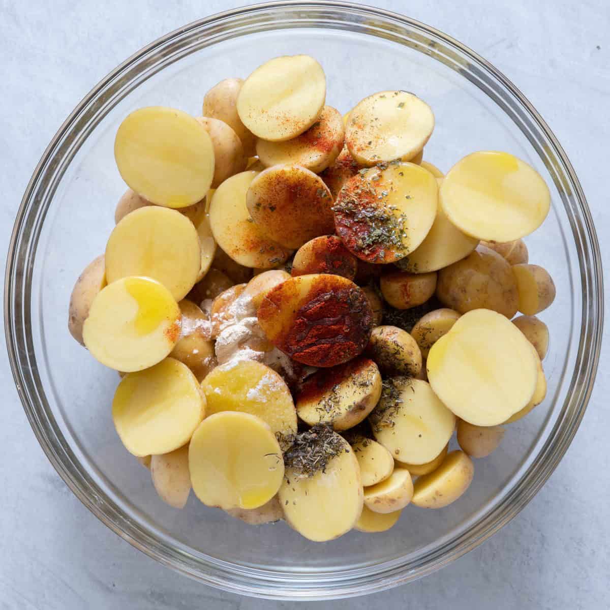Potatoes halved in large bowl, seasoning distributed, olive oil added.