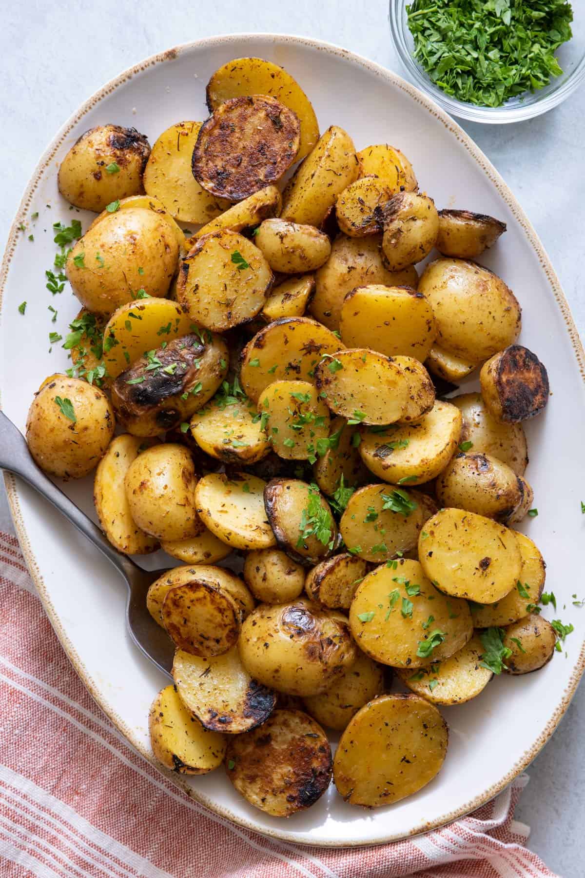 Platter with grilled potatoes garnished with parsley and spoon on side.