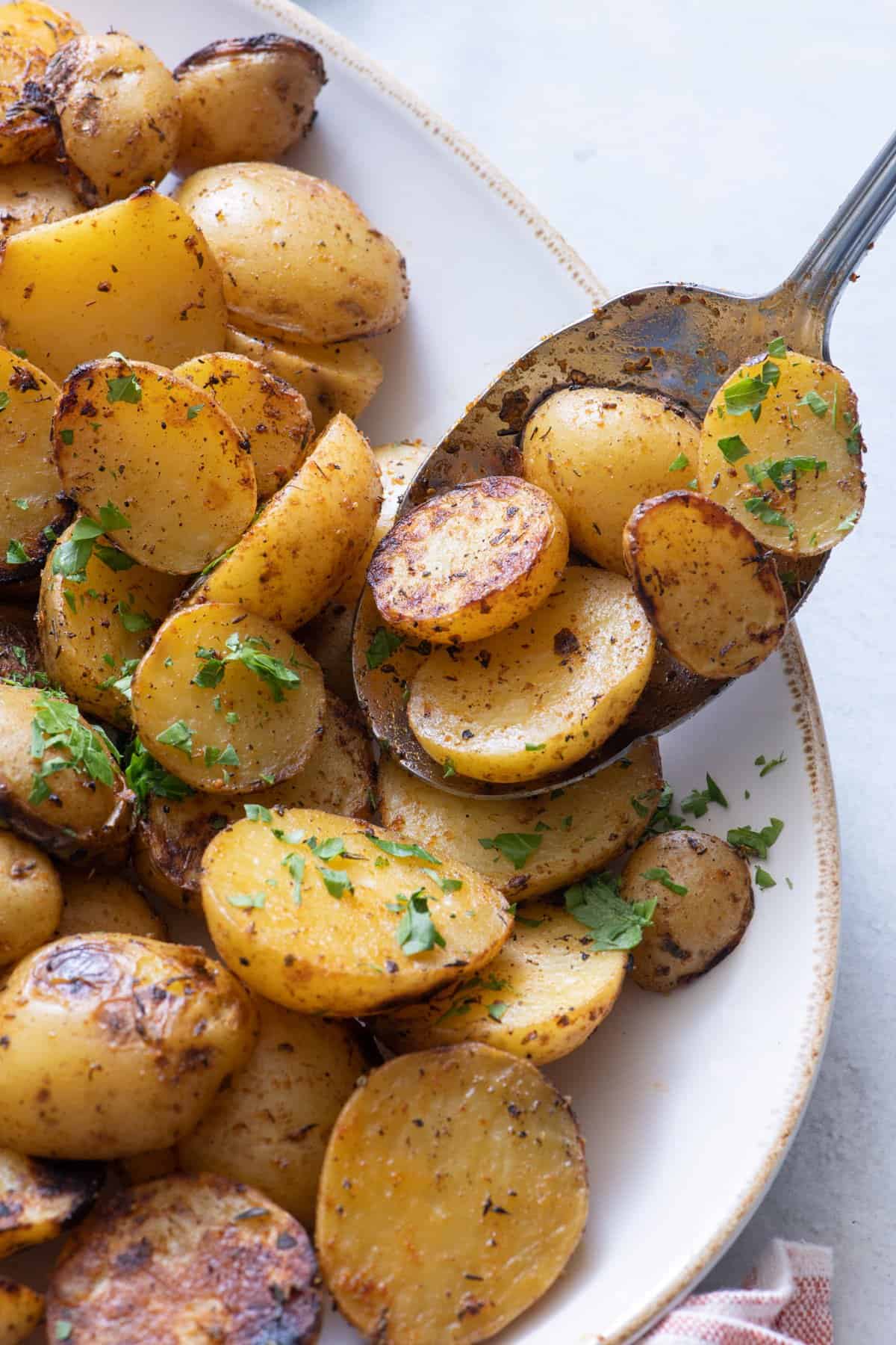Spoon grabbing seasoned grilled potatoes garnished with parsley from serving dish.
