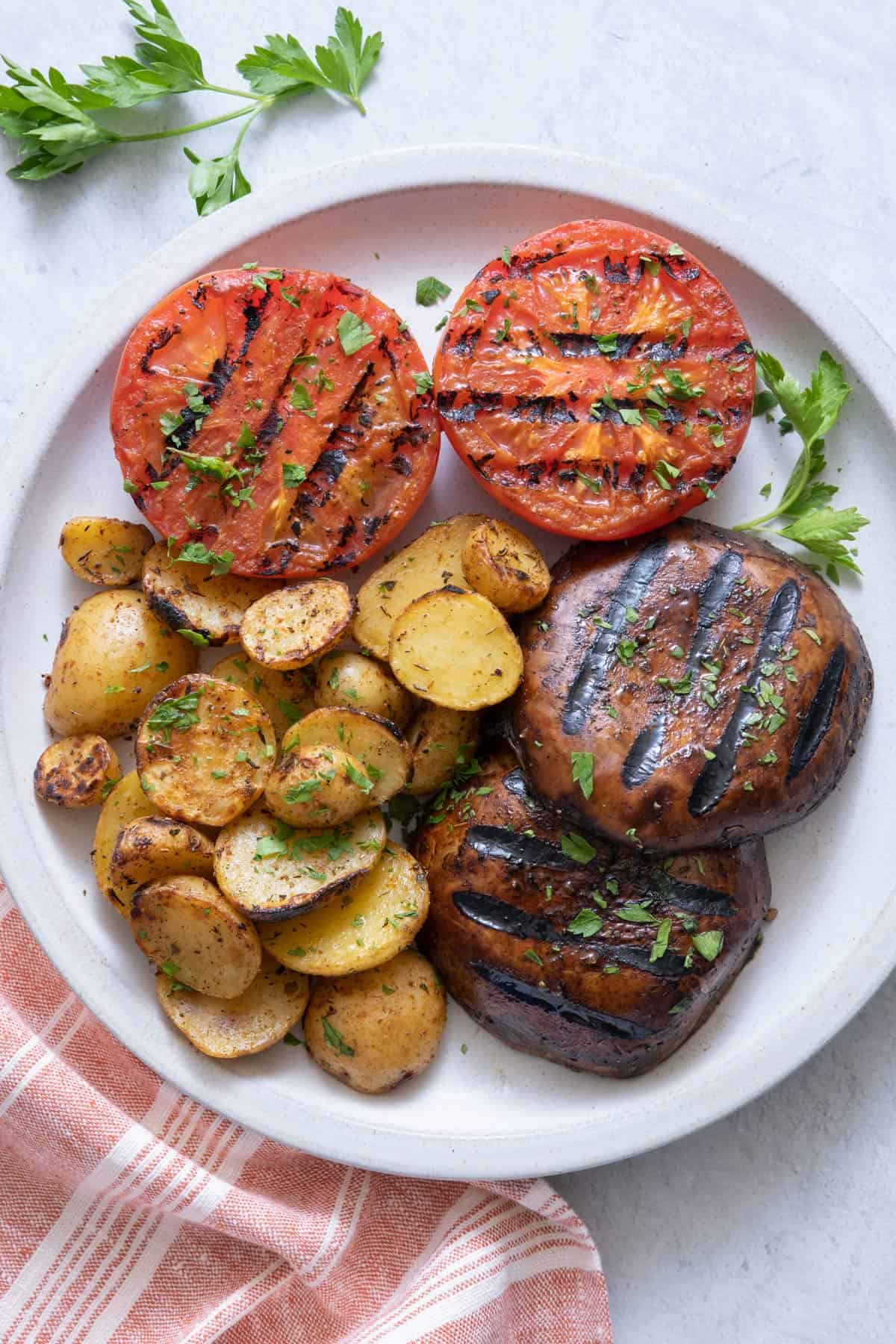 Plate with grilled potatoes, grilled tomatoes, and grilled portabella mushrooms, garnished with fresh parsley.