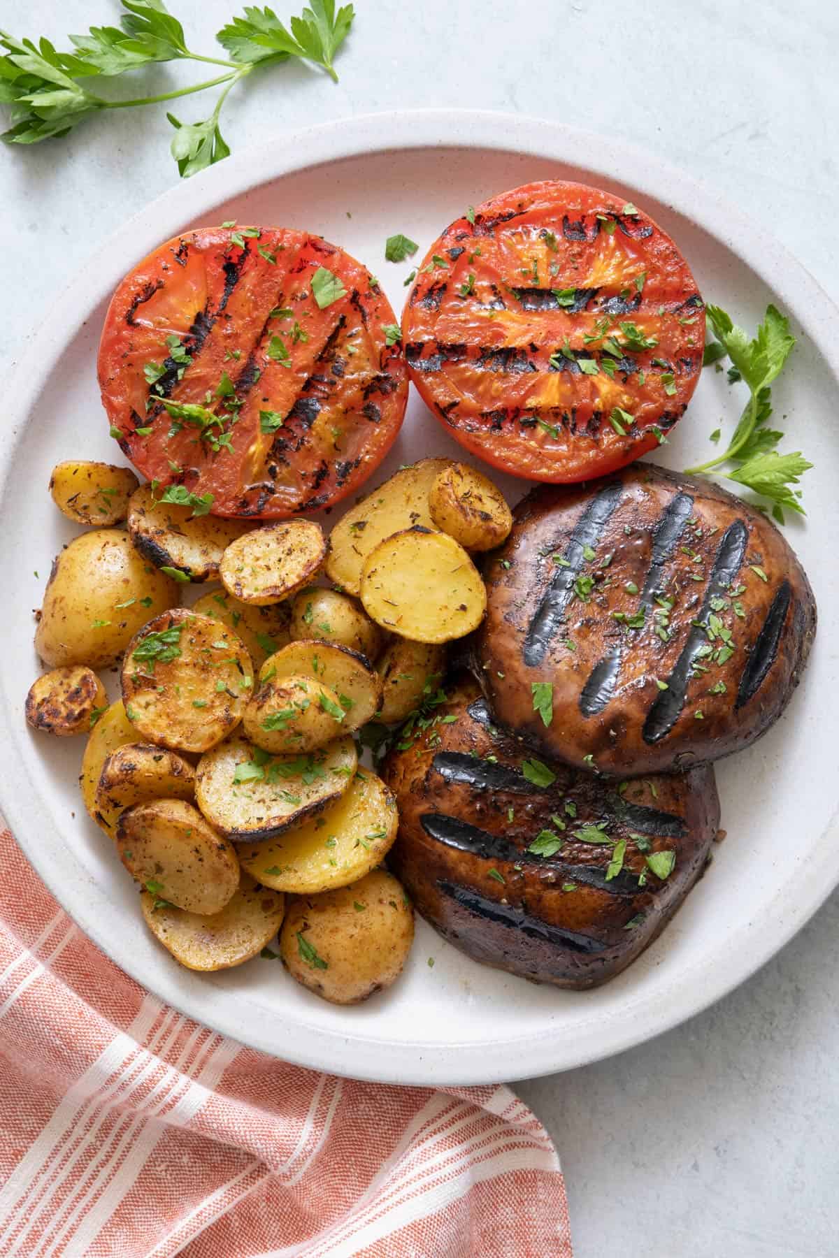 Large white plate with grilled tomatoes, grilled mushrooms, and grilled potatoes, garnished with parsley.