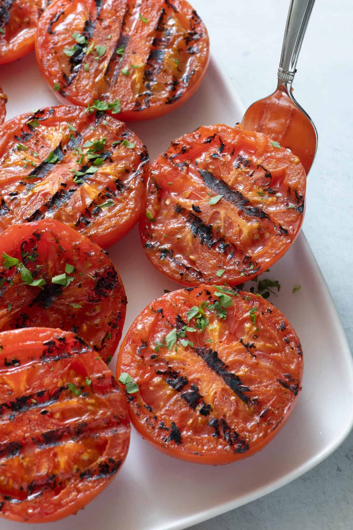 Close up of grilled tomatoes being lifted with a serving fork from plate.