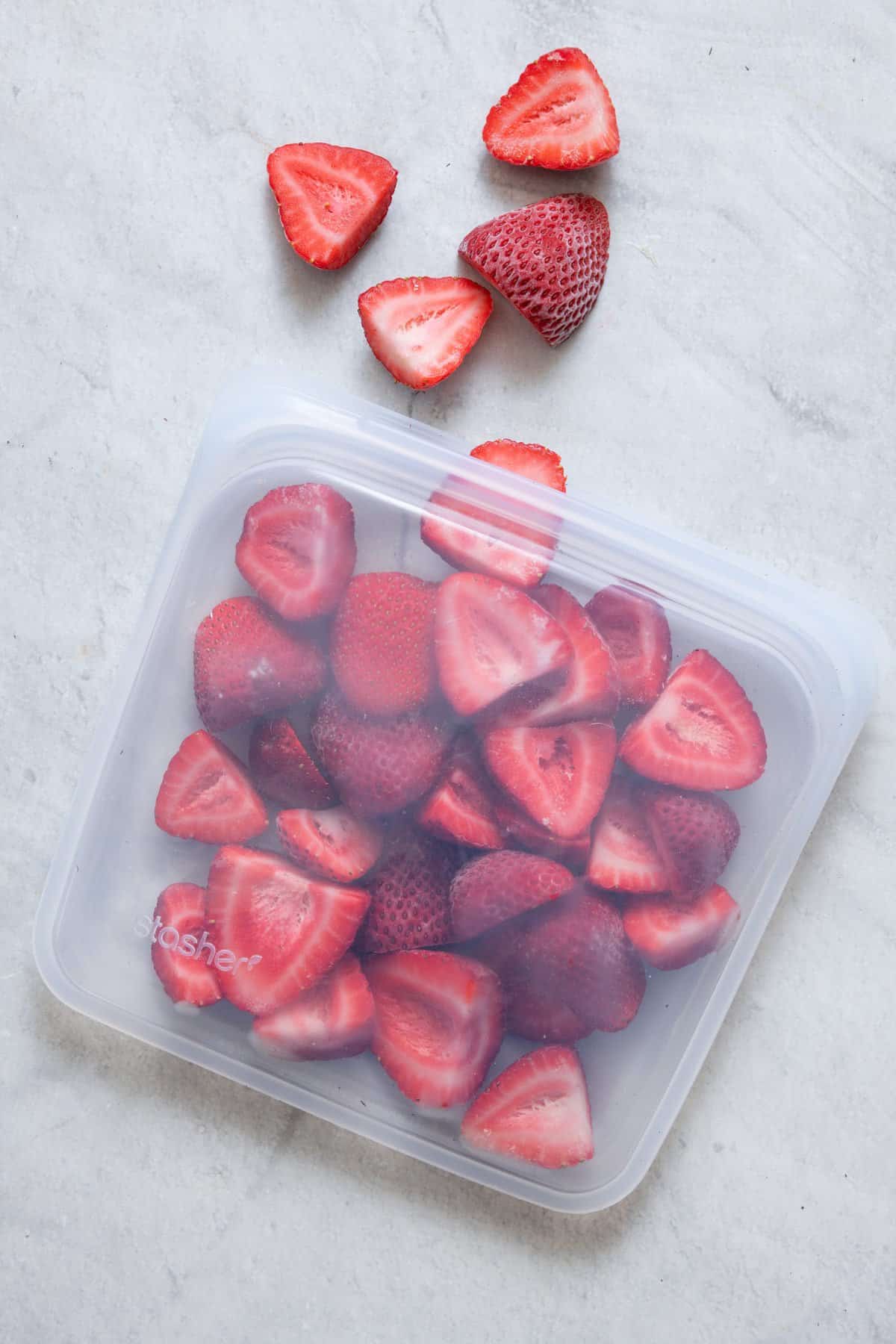 Frozen strawberries in a clear silicone bag laying on surface with a couple coming out.