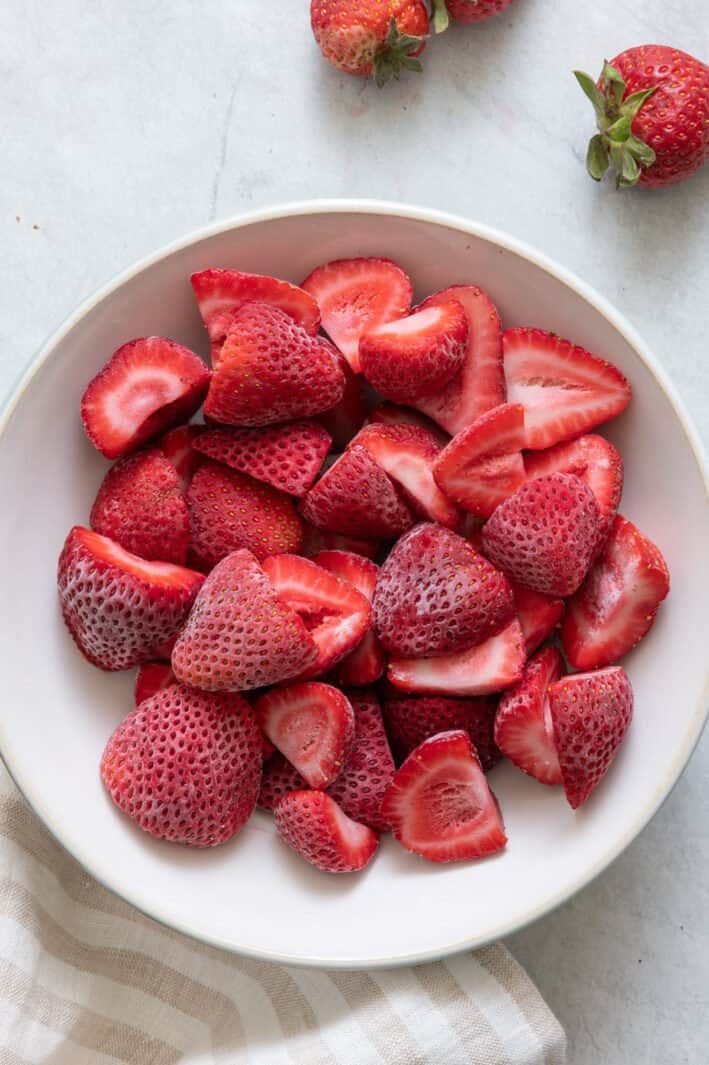 White bowl full of frozen halved strawberries.