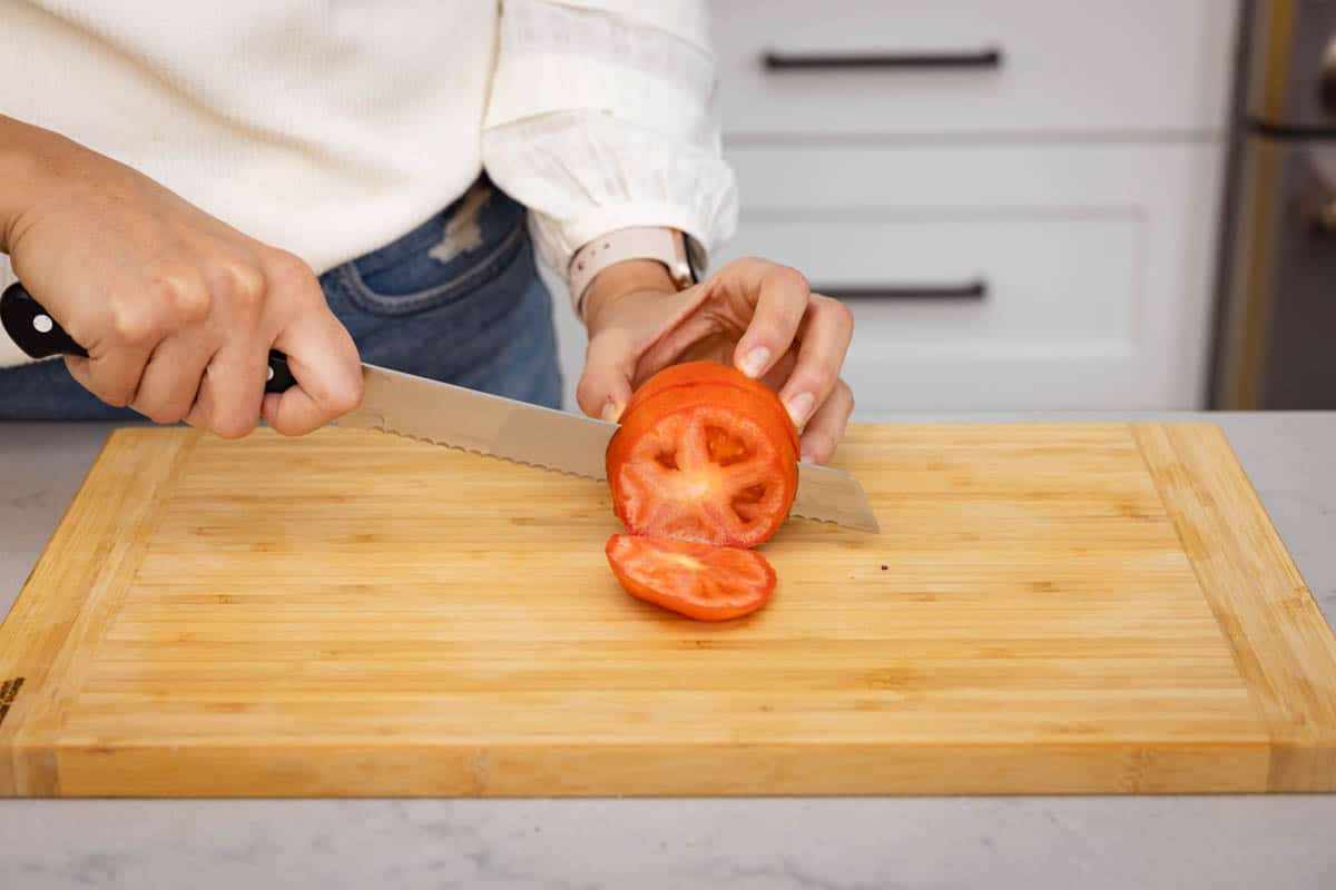 Serrated knife cutting tomato on cutting board