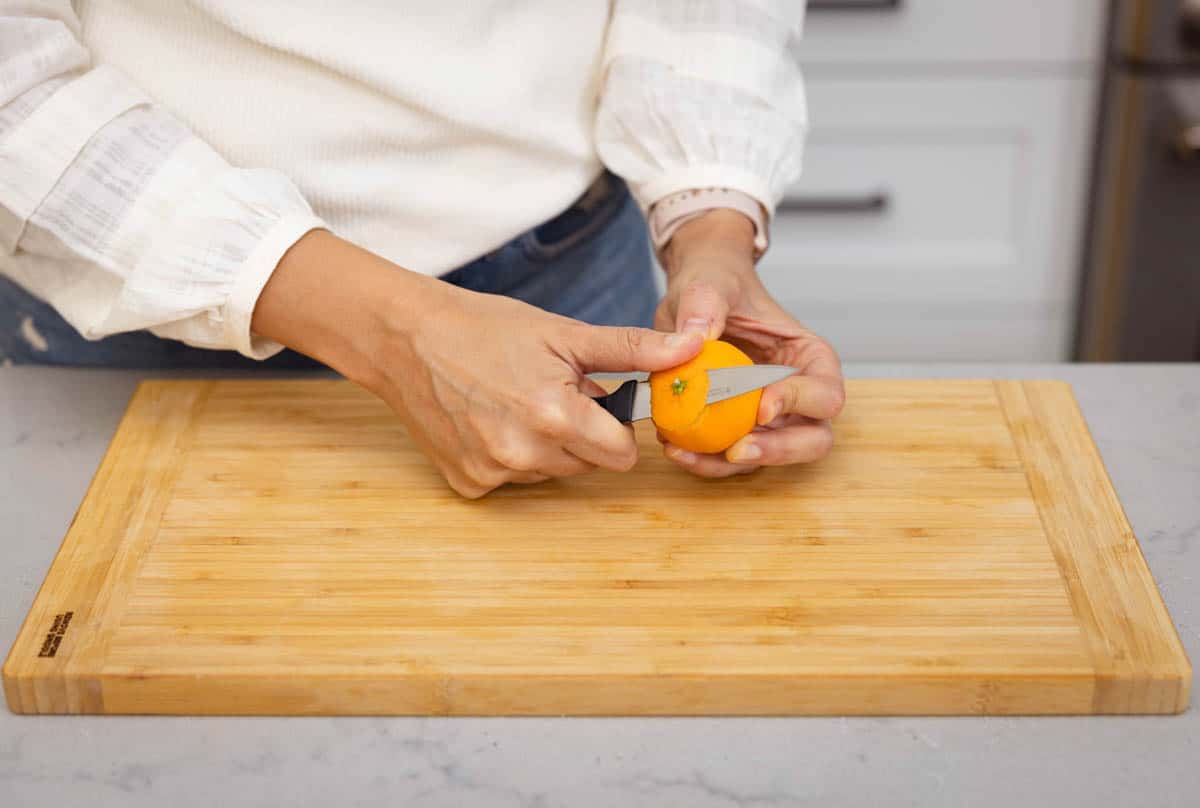 Paring knife peeling clementine over cutting board