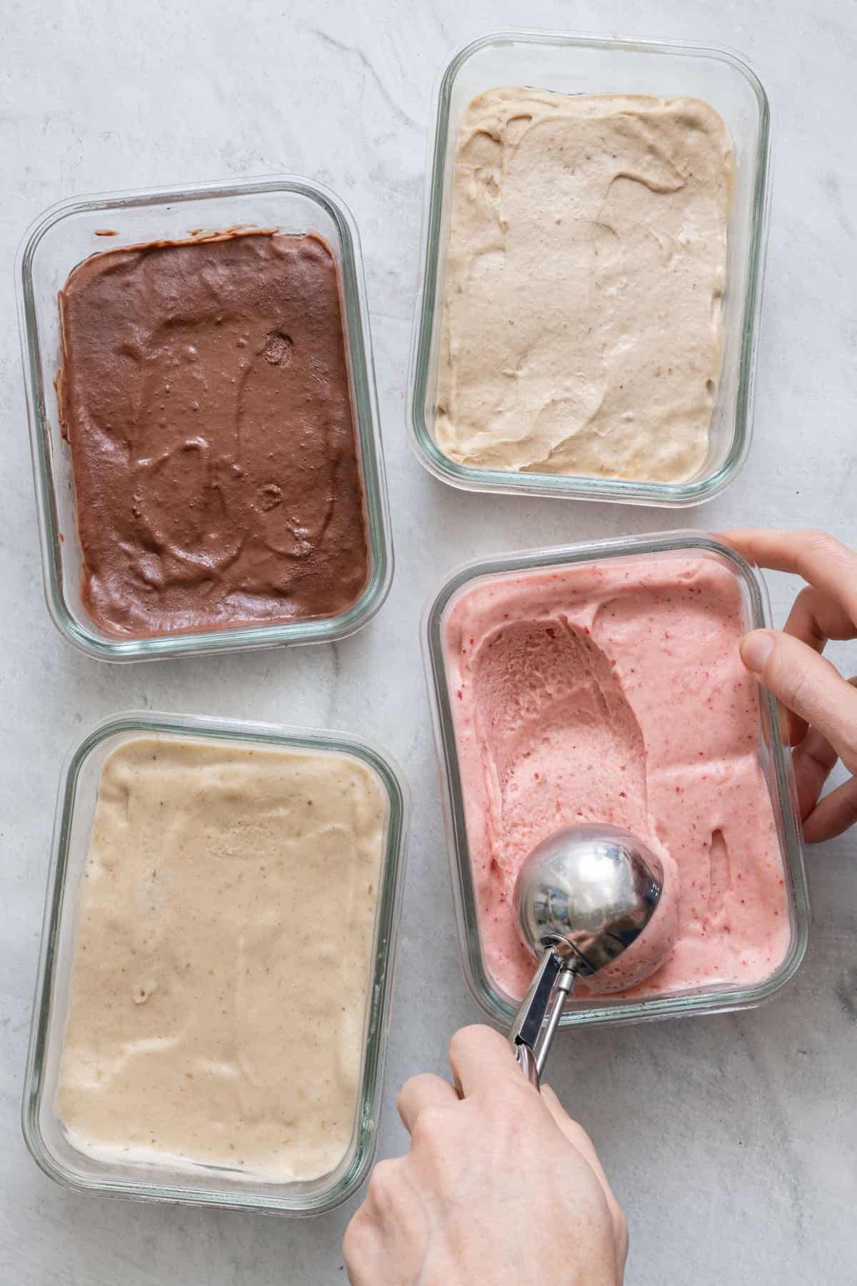 Nice cream four ways in freezer safe glass containers and a serving of strawberry nice cream being scooped out with an ice cream scooper.