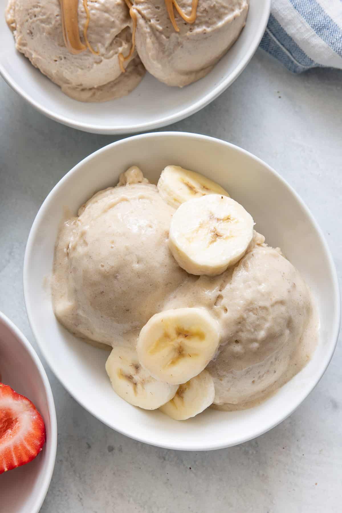 Banana vanilla Nice cream topped with banana slices with bowls of other flavored nice cream off to side.