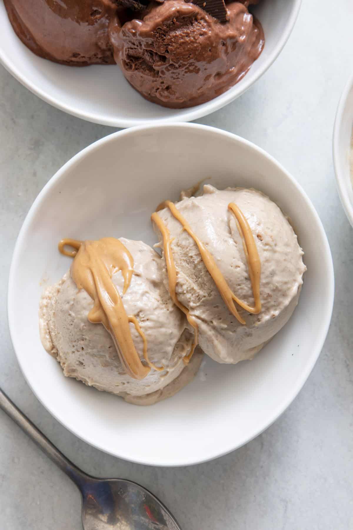2 scoops of Peanut butter Nice cream in a bowl with peanut butter drizzled on top and chocolate ice cream off to the side.