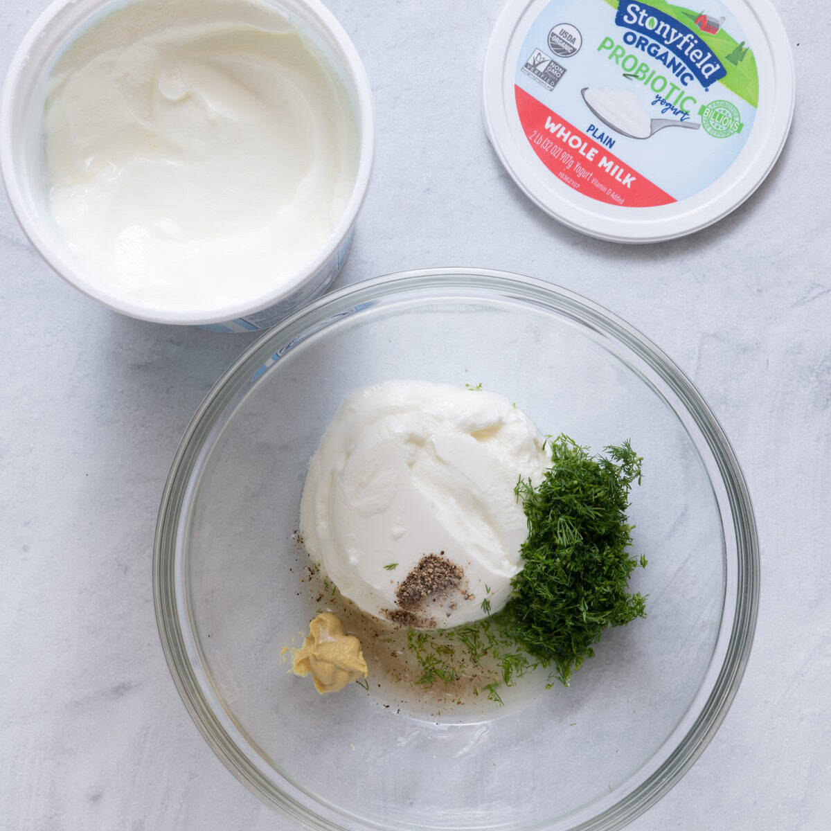 Bowl of Stonyfield yogurt, lemon juice, dill, dijon, salt and pepper before mixing.