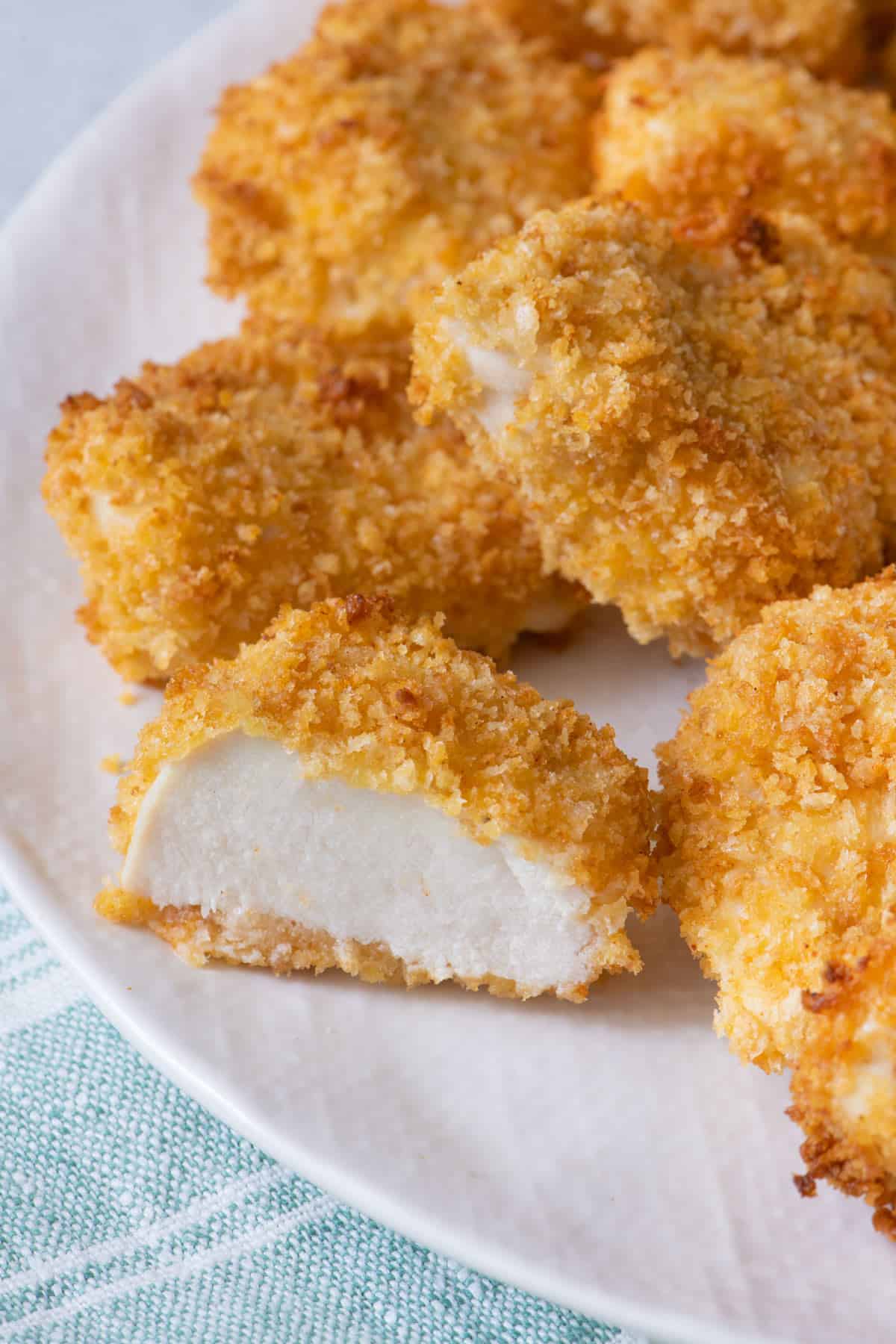 Close up shot of half of a plate of chicken nuggets with one cut open to show the inside of the chicken nugget.