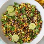 Large bowl of corn and bean salad with slices of lime and cilantro on top.