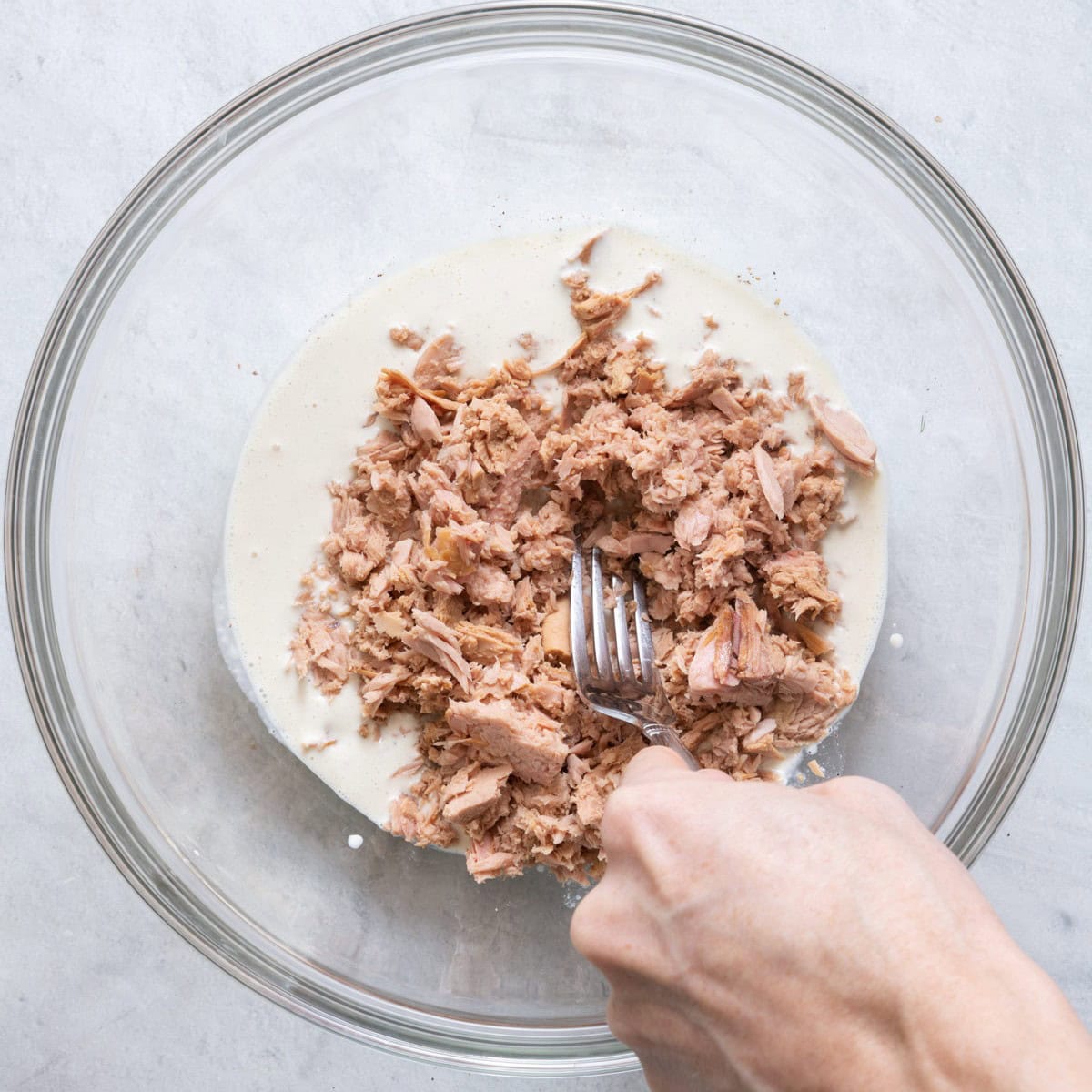 Breaking tuna with fork into dressing.