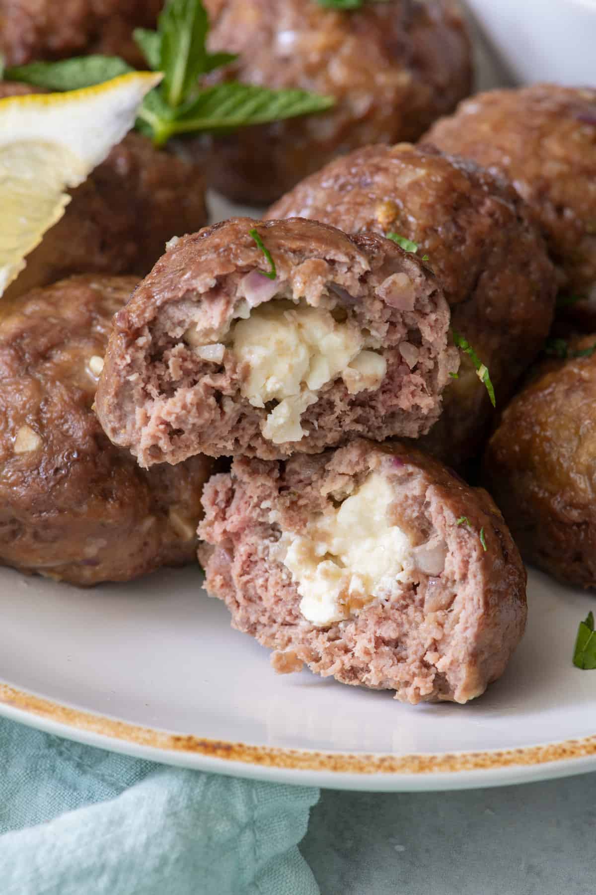 Close up of a plate of stuffed meatballs with one cut in half to show feta cheese inside.