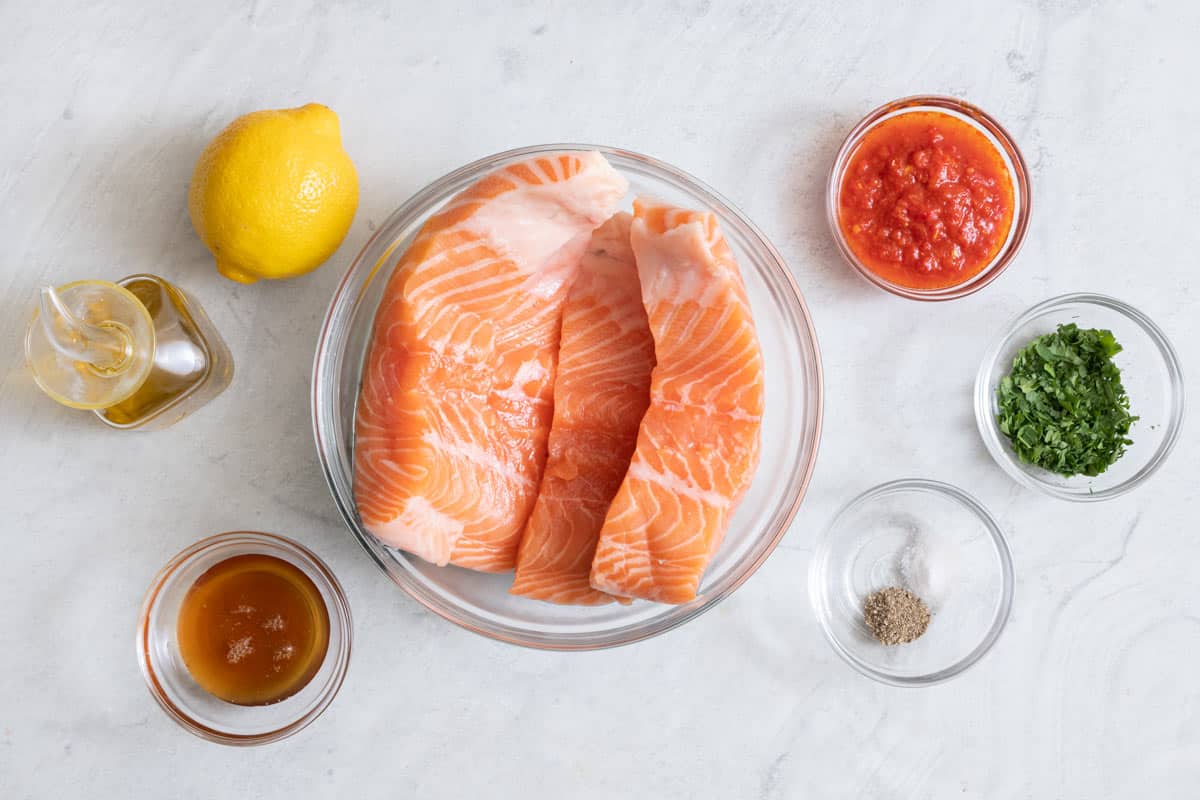 Ingredients for recipe using salmon fillets, oil, lemon, honey, harissa, an lemon.